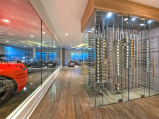 Contemporary wine cellar at car dealership featuring glass doors, wood & stainless steel accents.