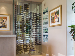 Custom glass wine cellar built to fit in small corner of wet bar area and designed to match modern decor.