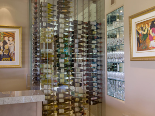 Custom glass wine cellar built to fit in small corner of wet bar area and designed to match modern decor.