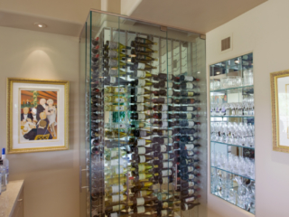 Custom glass wine cellar built to fit in small corner of wet bar area and designed to match modern decor.