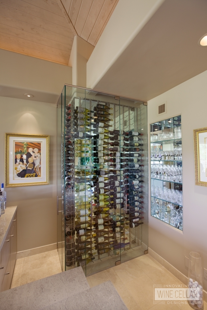 Custom glass wine cellar built to fit in small corner of wet bar area and designed to match modern decor.